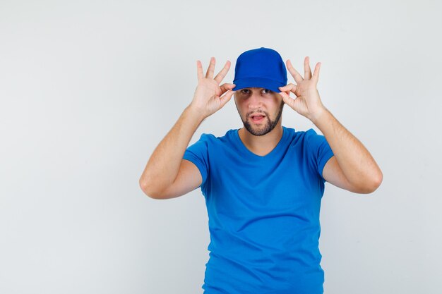 Jeune homme en t-shirt bleu tirant vers le bas sa casquette et à la cool