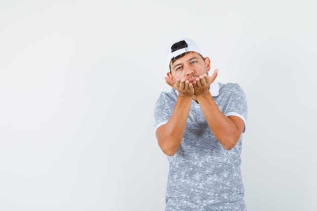 Photo gratuite jeune homme en t-shirt et casquette envoyant un baiser d'air et à la cool