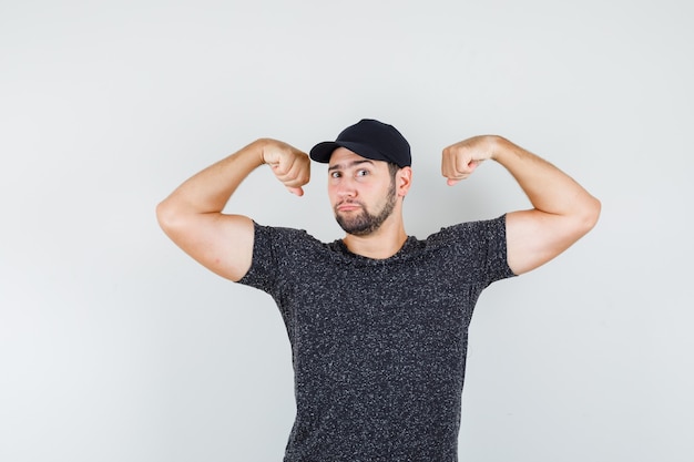 Jeune homme en t-shirt et casquette montrant les muscles et à la forte