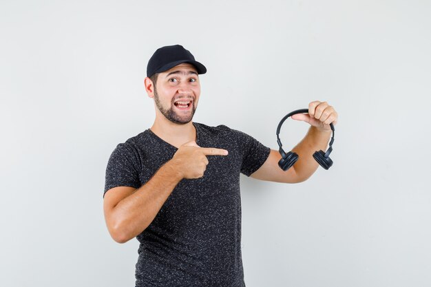 Jeune homme en t-shirt et casquette pointant sur les écouteurs et à la bonne humeur