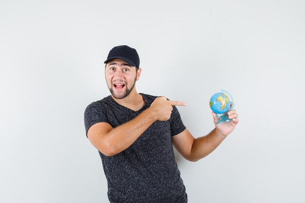 Jeune homme en t-shirt et casquette pointant sur globe et à la joyeuse