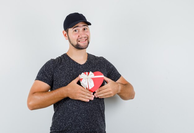 Jeune homme en t-shirt et casquette tenant présent fort et à la bonne humeur