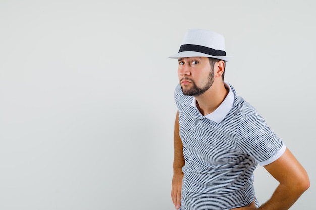 Jeune Homme En T-shirt, Chapeau Entendant Une Conversation Privée Et L'air Curieux, Vue De Face.