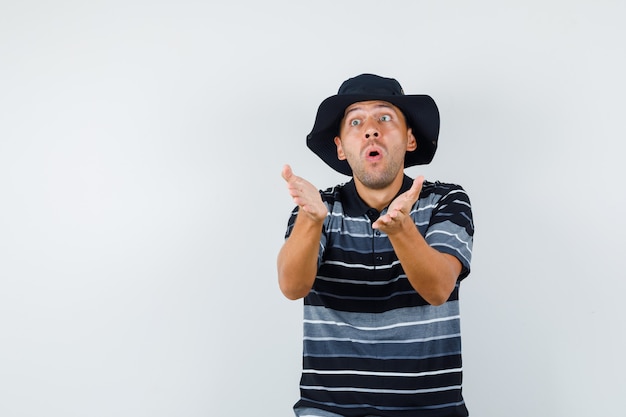 Jeune homme en t-shirt, chapeau essayant d'expliquer quelque chose et l'air excité, vue de face.