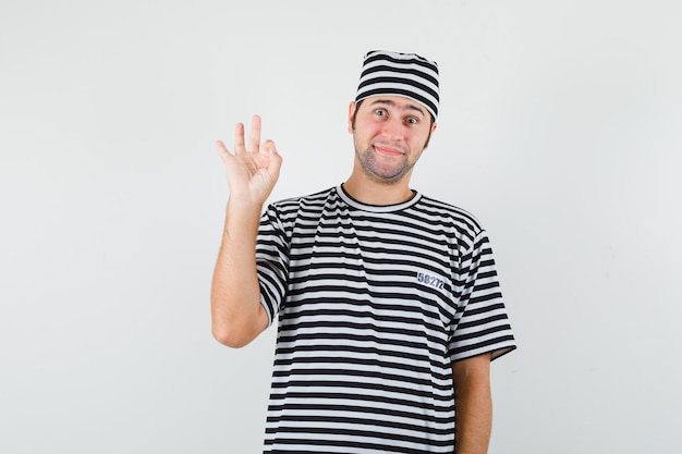 Jeune homme en t-shirt, chapeau montrant un geste correct et à la vue de face, joyeux.