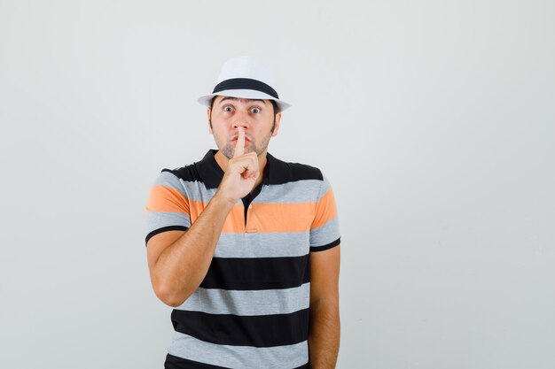 Jeune homme en t-shirt, chapeau montrant un geste silencieux et à l'attention