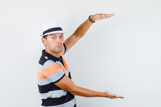 Jeune homme en t-shirt et chapeau montrant un signe de grande taille