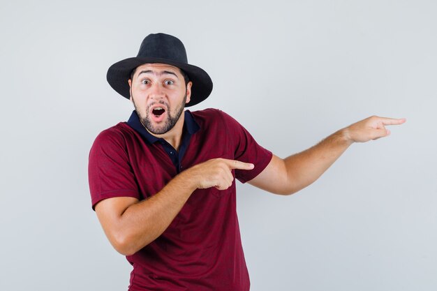 Jeune homme en t-shirt, chapeau pointant de côté et à la surprise, vue de face.