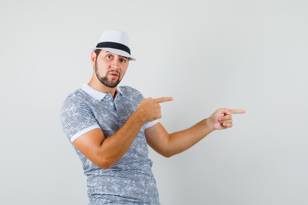 Jeune homme en t-shirt, chapeau pointant vers le côté et regardant prudemment, vue de face.