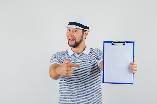 Jeune homme en t-shirt, chapeau pointant vers son ordinateur portable et à la vue de face, prêt.