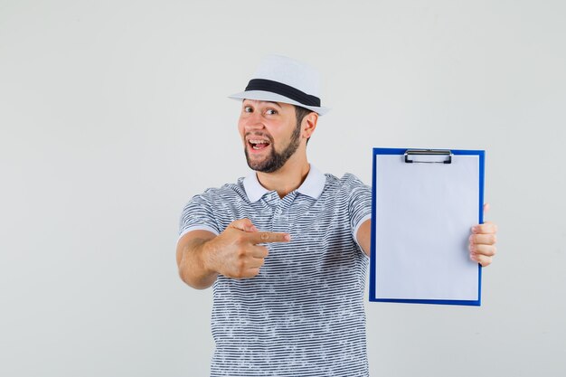 Jeune homme en t-shirt, chapeau pointant vers son ordinateur portable et à la vue de face, prêt.