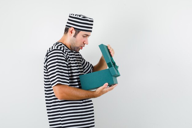 Jeune homme en t-shirt, chapeau à la recherche dans une boîte-cadeau et à la surprise.