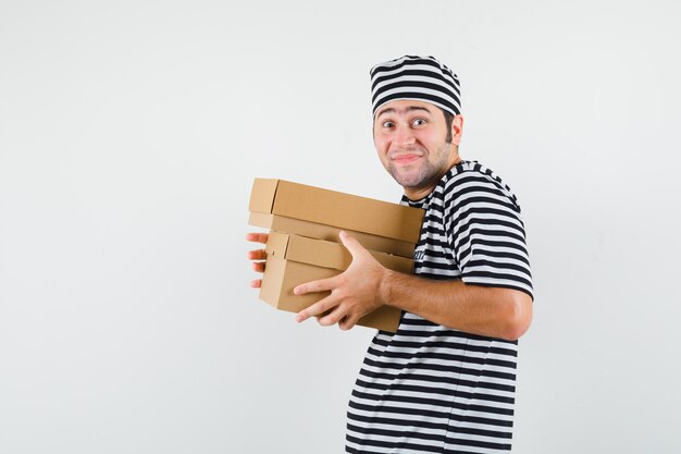 Jeune homme en t-shirt, chapeau tenant des boîtes en carton et à la bonne humeur.