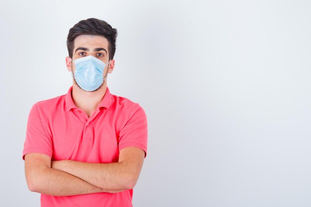 Jeune homme en t-shirt debout avec les bras croisés et l'air confiant, vue de face.