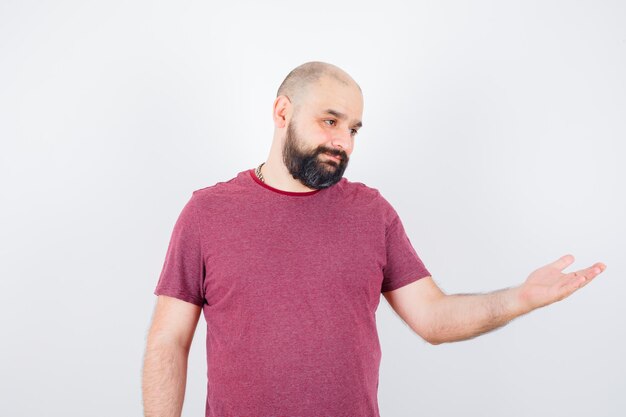 Jeune homme en t-shirt faisant semblant de montrer quelque chose et ayant l'air joyeux, vue de face.