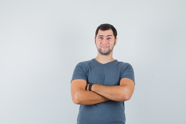 Jeune homme en t-shirt gris debout avec les bras croisés et à la confiance