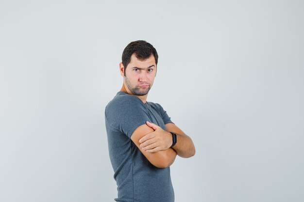 Jeune homme en t-shirt gris debout avec les bras croisés et à la douteuse