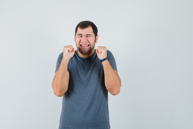 Jeune homme en t-shirt gris montrant le geste du gagnant et l'air heureux