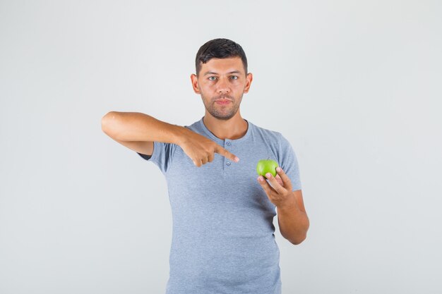 Jeune homme en t-shirt gris pointant le doigt sur la pomme verte