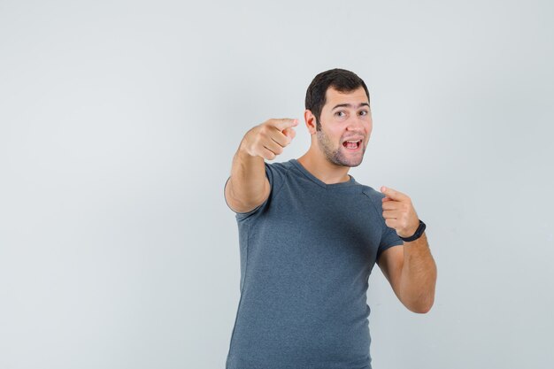 Jeune homme en t-shirt gris pointant vers la caméra et à la confiance