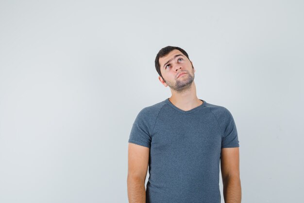 Jeune homme en t-shirt gris regardant vers le haut et à la pensif