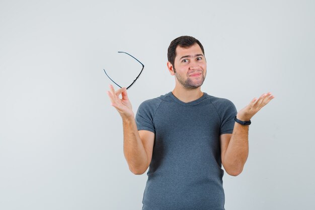 Jeune homme en t-shirt gris tenant des lunettes étalant la paume et à l'optimiste