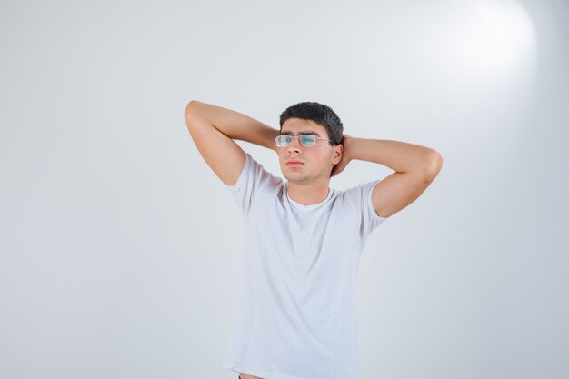 Jeune homme en t-shirt, main dans la main derrière la tête et à la vue détendue, de face.