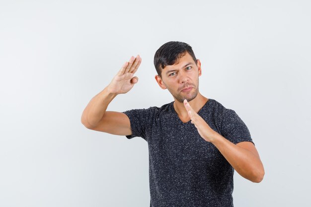 Jeune homme en t-shirt montrant le geste de la coupe de karaté et l'air confiant, vue de face.