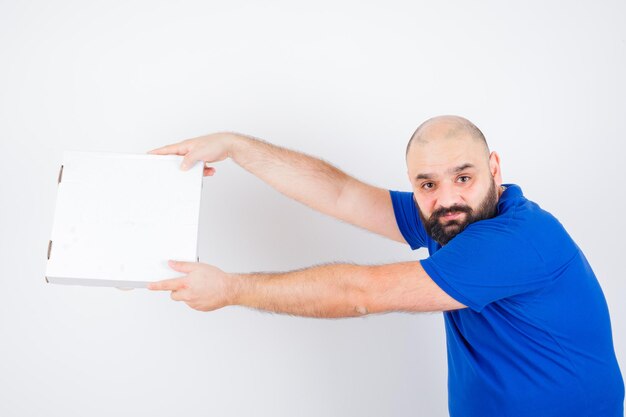 Jeune homme en t-shirt montrant le geste de donner et l'air joli, vue de face.