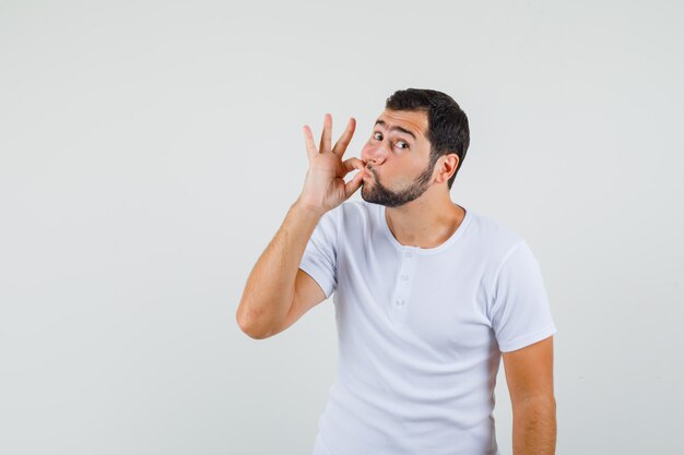 Jeune homme en t-shirt montrant le geste de la fermeture éclair et à la vue calme, de face.