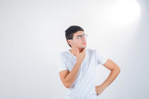 Jeune homme en t-shirt montrant en pensée pose et à la vue réfléchie, de face.