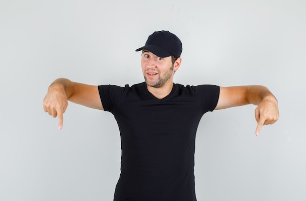 Photo gratuite jeune homme en t-shirt noir, casquette pointant vers le bas des doigts et à la curiosité