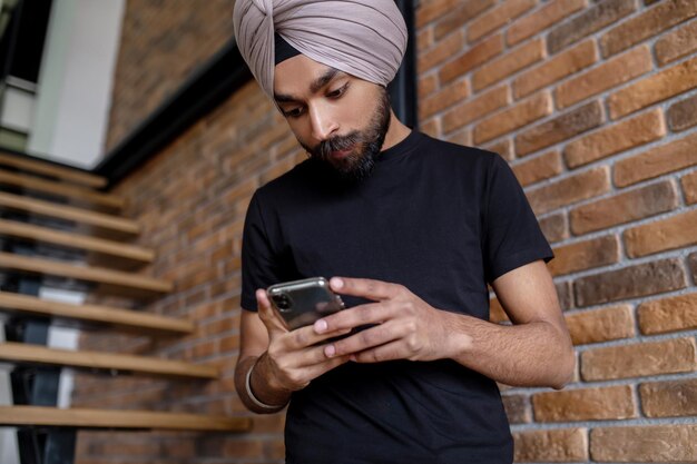 Jeune homme en t-shirt noir envoyant des SMS au téléphone et ayant l'air impliqué