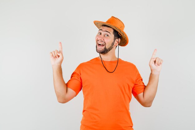 Jeune homme en t-shirt orange, chapeau pointant les doigts vers le haut et l'air optimiste, vue de face.