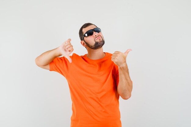 Jeune homme en t-shirt orange montrant les pouces de haut en bas et l'air confus, vue de face.