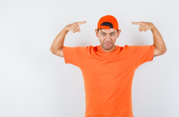 Photo gratuite jeune homme en t-shirt orange pointant sur sa casquette et à la confiance