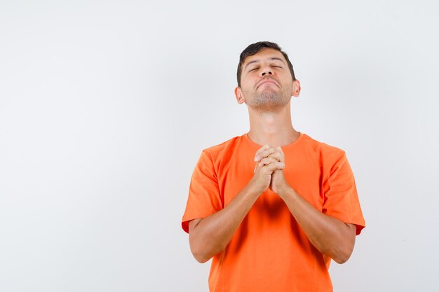 Jeune homme en t-shirt orange, serrant les mains en geste de prière et à l'espoir