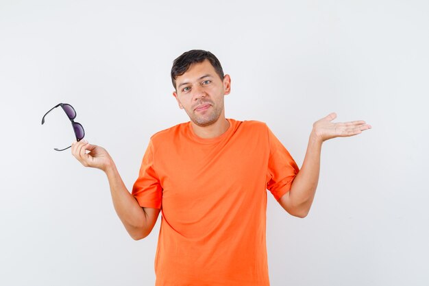 Jeune homme en t-shirt orange tenant des lunettes et à la confusion