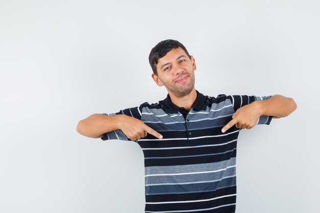 Jeune homme en t-shirt pointant vers le bas et l'air joyeux, vue de face.