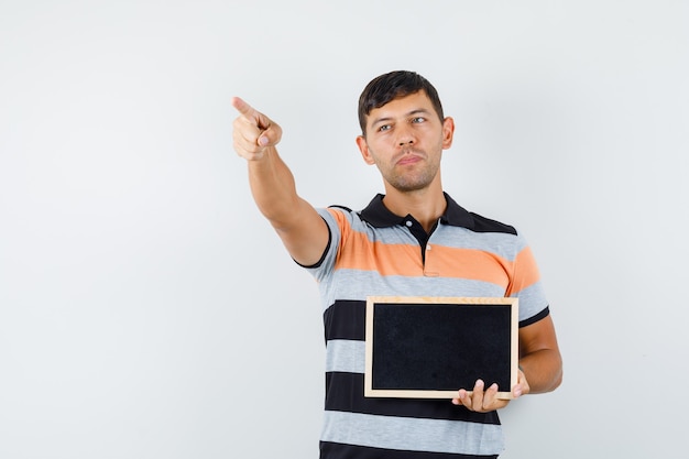 Jeune homme en t-shirt pointant vers l'extérieur tout en tenant le tableau noir et à la recherche concentrée