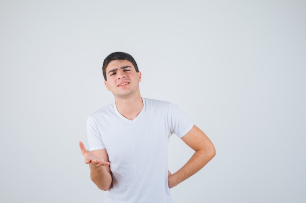 Jeune homme en t-shirt qui s'étend de la main en geste de questionnement et à la vue de face, confiant.