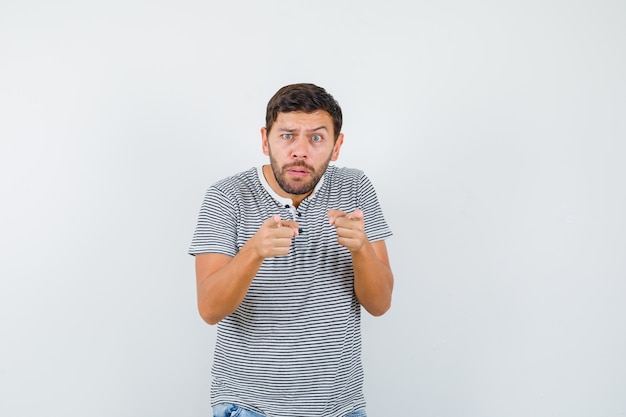 Jeune homme en t-shirt rayé pointant vers l'avant et à la perplexité , vue de face.