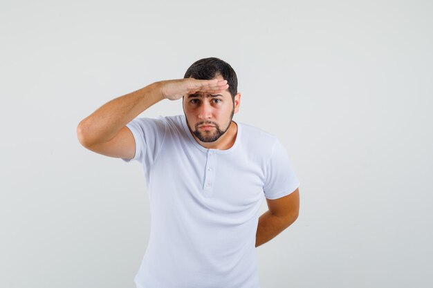 Jeune homme en t-shirt à la recherche de quelqu'un et regardant attentivement, vue de face.