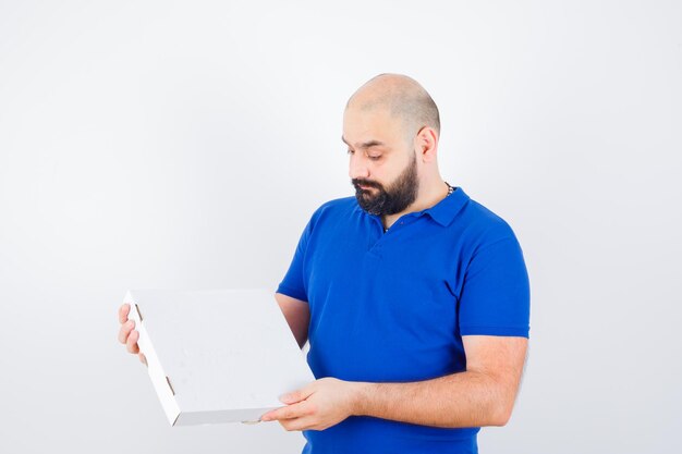 Jeune homme en t-shirt regardant une boîte à pizza fermée et ayant l'air confiant, vue de face.