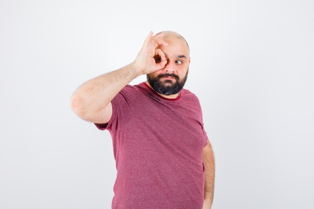 Jeune homme en t-shirt rose faisant le tour de ses yeux, vue de face.