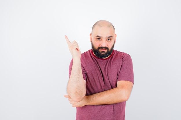 Jeune homme en t-shirt rose levant l'index en geste eurêka et semblant sensible, vue de face.