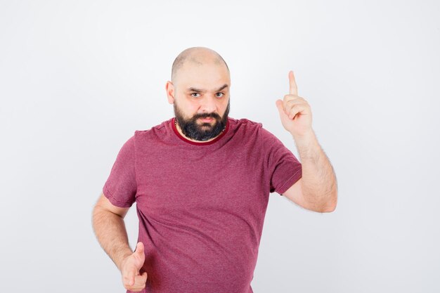 Jeune homme en t-shirt rose pointant vers le haut et regardant concentré, vue de face.