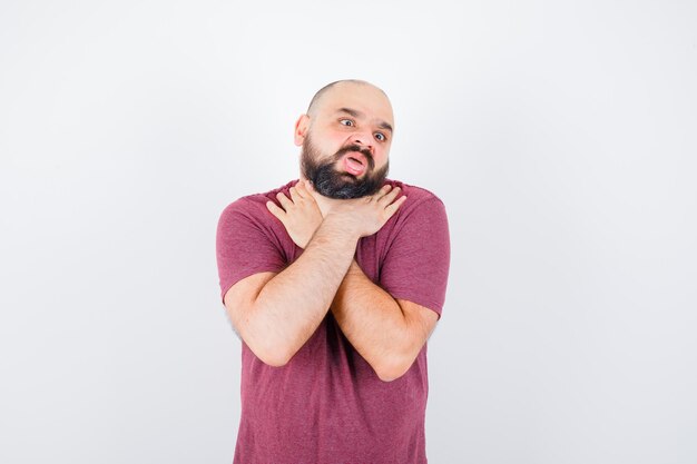 Jeune homme en t-shirt rose s'étranglant, vue de face.