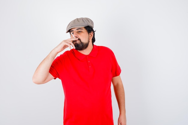 Jeune homme en t-shirt rouge, casquette fumeur, vue de face.