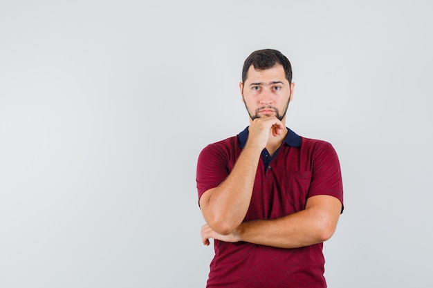 Jeune homme en t-shirt rouge avec impatience et à la vue de face, concentré.